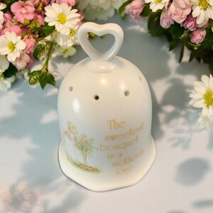 May include: White porcelain bell with a heart-shaped handle. The bell has a floral design and the text "The sweetest bouquet is a mother's love".