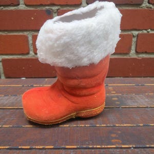 May include: An orange plush Christmas boot with a white faux fur cuff and gold trim. The boot is sitting on a wooden surface. The boot is a festive decoration.