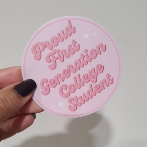 May include: Pink round sticker with the text "Proud First Generation College Student" in a pink retro font with white sparkles.