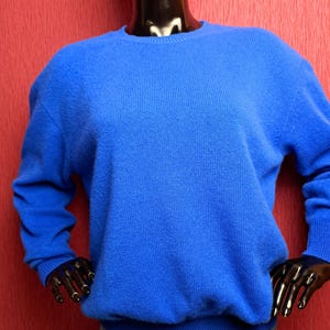 Pode incluir: Um suéter de malha azul brilhante com mangas compridas e gola redonda.