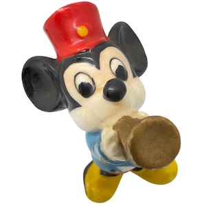 May include: A vintage ceramic Mickey Mouse figurine in a band uniform. The figurine has a red hat with a yellow button, a blue jacket, yellow shoes, and a brown horn. The classic Disney character is in a playful pose.