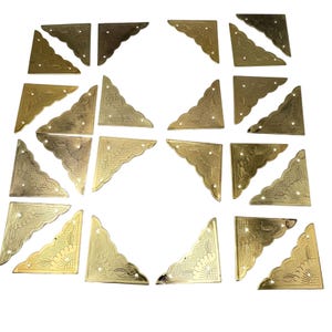 May include: A collection of brass-colored corner brackets with decorative floral and leaf patterns. Each bracket has a triangular shape with multiple screw holes for secure attachment. The brackets vary slightly in design and finish.
