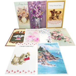 Puede incluir: Una colección de ocho tarjetas de felicitación rectangulares con diversas ilustraciones, incluyendo arreglos florales, dos cachorros, un águila calva con un escudo de la bandera estadounidense, un faro en un acantilado y un perro con un sobre rojo.
