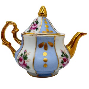 May include: A porcelain teapot featuring alternating white and light blue vertical panels. The white panels are decorated with pink rose floral motifs, while the blue panels feature gold dot and leaf accents. It has a gold handle, spout, and lid.