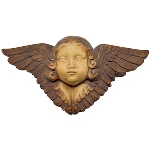 May include: A carved wooden angel with a serene expression and detailed wings. The angel's face is a light tan color, contrasting with the darker brown wings. This decorative piece is likely for wall decor.