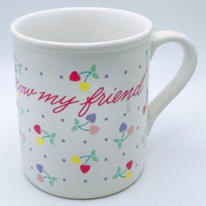 May include: White ceramic mug with a curved handle, decorated with colorful heart and floral patterns. The mug features the handwritten text "now my friend" in red cursive, with small polka dots scattered across the surface.