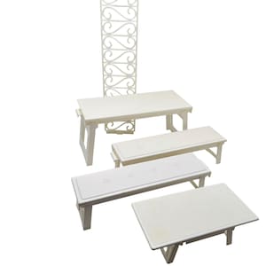 May include: A collection of miniature white benches and a decorative trellis. The benches vary in size and design, some with cushioned seats and others with solid tops. The trellis features an ornate, repeating scrollwork pattern.