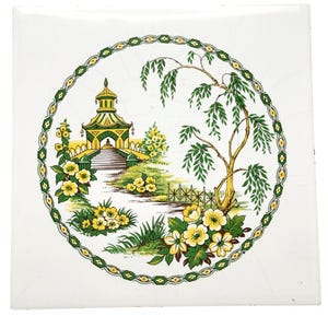 May include: A square white ceramic tile featuring a circular decorative border in green and yellow. The center illustration depicts a yellow pagoda, a weeping willow tree, and clusters of yellow flowers with green leaves on a grassy landscape.