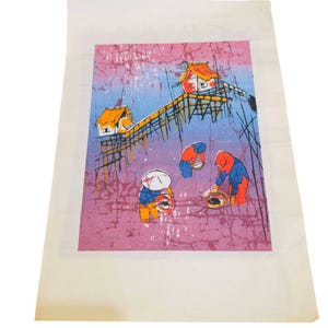 May include: A colorful batik print depicting a coastal scene with small houses on stilts and figures working with baskets. The artwork features a palette of pink, blue, orange, and white, with a textured background.
