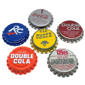 May include: Six vintage metal bottle caps featuring various soda brand logos including Coca-Cola, RC, Double Cola, C&C Super Coola, and Tab. Each cap displays specific brand text, ingredients, and manufacturing details printed on the top surface.