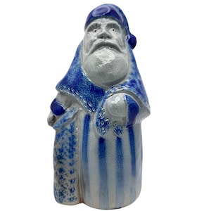 Puede incluir: Figura de cerámica de Papá Noel en tonos azules y blancos. La figura lleva un gorro y una túnica azules con detalles intrincados. Rayas azules verticales adornan el cuerpo, con un aspecto rústico y artesanal. Una decoración festiva para las fiestas.