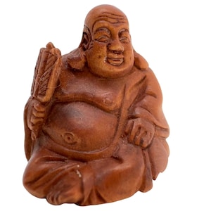 May include: A small, carved wooden figurine of a seated, smiling figure with a bald head and a large belly. The figure is depicted in a cross-legged position, holding a fan in the right hand and wearing robes that drape over the body.