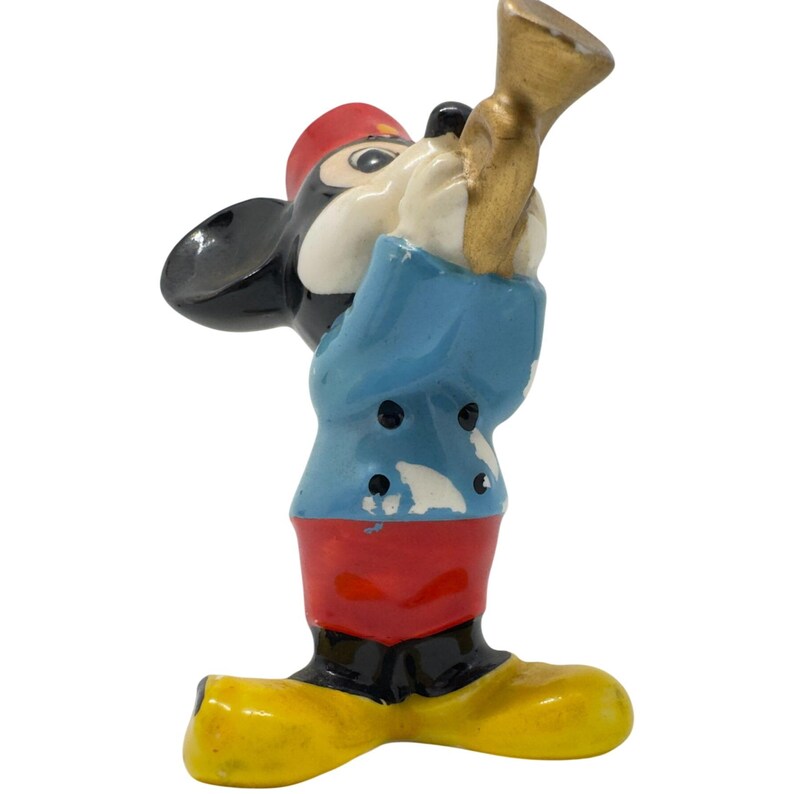 May include: A vintage Mickey Mouse figurine in a band uniform, playing a gold trumpet. The figurine has a red hat, blue jacket, red trousers, black shoes, and yellow feet. A collectible item.