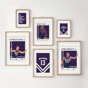 May include: A collection of framed prints featuring Fremantle Dockers players. Each print has a gold frame and a dark purple background. The prints include player names, numbers, and action shots, with the team's logo and inspirational quotes.