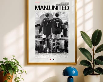 May include: A framed poster with a gold border featuring two soccer players in black jerseys with the text "MAN.UNITED." The players are standing with their backs to the viewer. The poster includes additional text at the top and bottom.