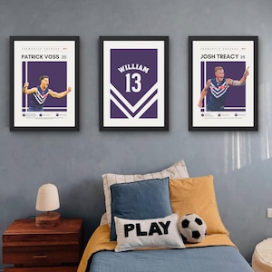 Könnte beinhalten: Drei gerahmte Wandbilder mit Motiven des Australian Rules Football Teams Fremantle Dockers. Zwei Bilder zeigen die Spieler Patrick Voss und Josh Treacy in Trikots, während das mittlere Bild ein violettes Trikot mit dem Namen William und der Nummer 13 zeigt.