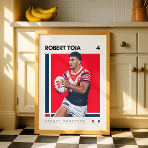 May include: A framed poster featuring a digital illustration of rugby player Robert Toia wearing a Sydney Roosters jersey, holding a rugby ball, with the text Robert Toia, the number 4, and Sydney Roosters printed on a white background.