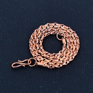 Könnte beinhalten: Eine Kupferkette mit einem Karabinerverschluss und einem kleinen Ring am Ende. Die Kette besteht aus kleinen, gedrehten Gliedern.