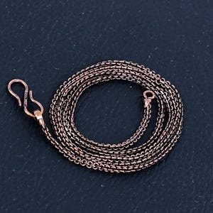 Puede incluir: Un collar de cadena de cobre con cierre de mosquetón. La cadena está hecha de pequeños círculos unidos.