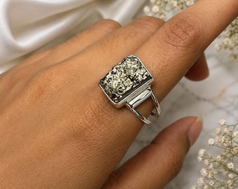 May include: A silver ring featuring a rectangular, metallic, textured pyrite stone set in a polished metal frame. The band consists of two thin, parallel silver wires that connect to the base of the stone setting, creating a clean, open design.