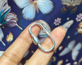 May include: A silver oval-shaped lobster clasp with a smooth, polished finish. The clasp is designed for attaching jewelry or other accessories.