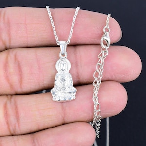 Puede incluir: Collar con colgante de plata que representa a un Buda sentado en detalle. La cadena es de plata y tiene un cierre de langosta.