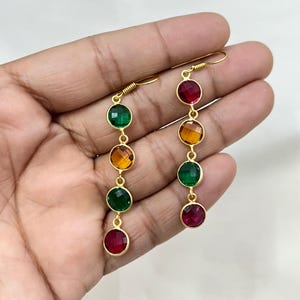 Pode incluir: Brincos de argola dourados com quatro pedras redondas. As pedras preciosas são vermelhas, verdes e âmbar.
