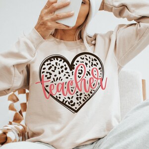 May include: A beige sweatshirt with a leopard print heart and the word "teacher" in pink lettering.