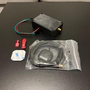 May include: A black rectangular electronic device with a gold-colored connector, red and green wires, and a black cable with a rounded component. Also included are red and pink connectors and a white adhesive pad.