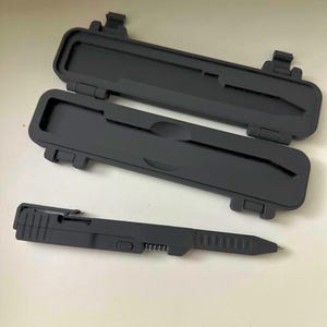 May include: Black pen and case set. The pen is black with a silver tip and a clip. The case is black and opens to reveal a compartment for the pen. The case has a hinged lid and a secure latch.