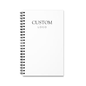 May include: A white, spiral-bound notebook featuring the text "CUSTOM LOGO" in black. The notebook has a black spiral binding along the left edge.