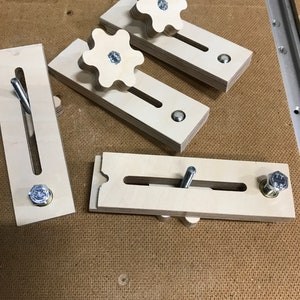 May include: Four wooden clamps with star-shaped knobs and metal screws. The clamps are made of light wood and have a natural finish.