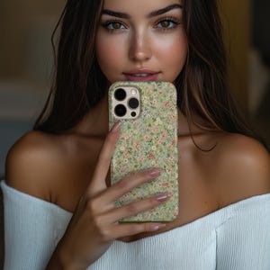 May include: A smartphone case featuring a light green background with a dense, repeating pattern of tiny pink, white, and yellow flowers. The case has a rectangular cutout for a triple-lens camera system and a flash, with a raised edge around the lenses.