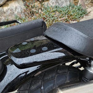 Peut inclure: Motocyclette noire avec une selle en cuir noir et une sacoche en cuir noir. La motocyclette a un pot d'échappement chromé et un garde-boue arrière chromé.