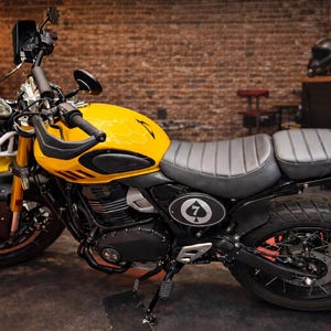 May include: A yellow and black motorcycle with a black seat and tires. The motorcycle has a black windshield and handlebars. The gas tank has a black and white emblem with the number 7 and a spade symbol.