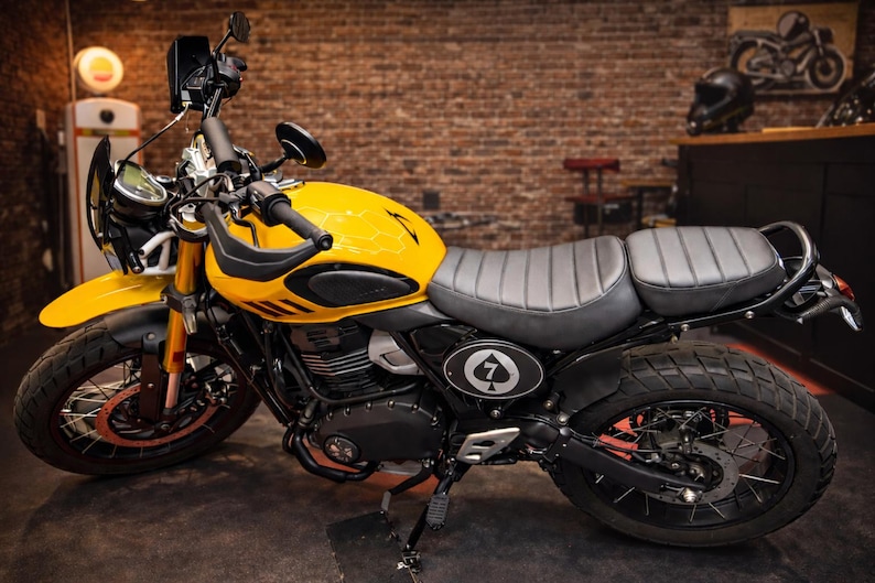 May include: A yellow and black motorcycle with a black seat and tires. The motorcycle has a black windshield and handlebars. The gas tank has a black and white emblem with the number 7 and a spade symbol.