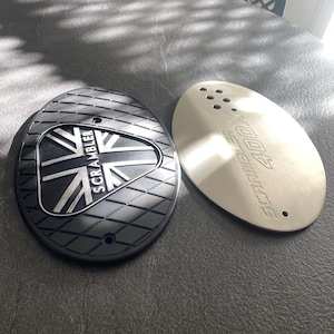 May include: Two motorcycle parts. One is black with a diamond pattern and the Union Jack flag and the word "SCRAMBLER". The other is silver with the words "SCRAMBLER 400X".