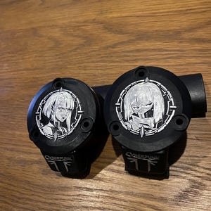 May include: Two black circular motorcycle brake reservoir covers featuring silver-toned engraved anime-style character portraits within a circular frame. Each cover displays the text CYBERPUNK and a logo at the bottom, with three mounting holes.