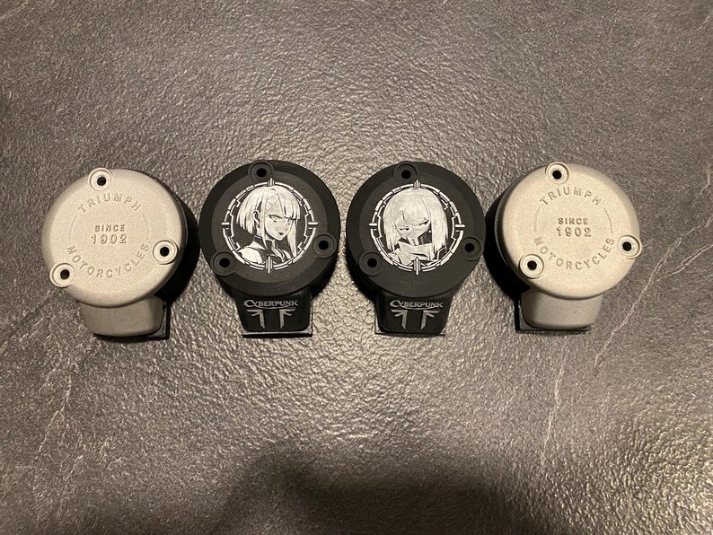 May include: Four circular motorcycle reservoir covers arranged in a row. Two silver covers feature the text Triumph Motorcycles Since 1902. Two black covers feature white anime-style character illustrations and the text Cyberpunk at the base.