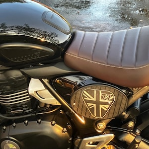 May include: Close-up of a black motorcycle with a brown leather seat. The motorcycle has a Union Jack emblem with the number 77 on the side. The motorcycle is parked outside.