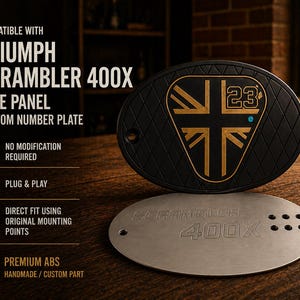May include: Black and gold Triumph Scrambler 400X side panel custom number plate. The oval-shaped plate features a gold emblem with the number 23 and a diamond pattern. A silver plate with the text "Scrambler 400X" is below.