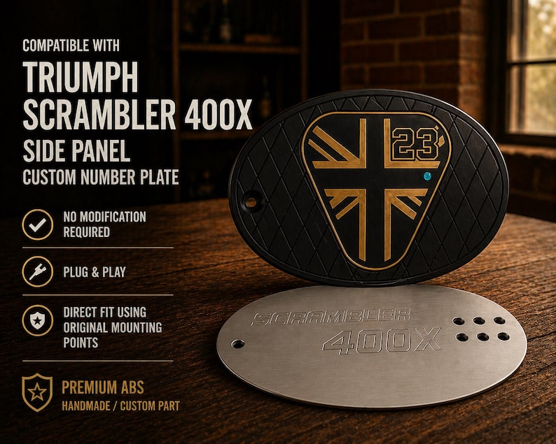 May include: Black and gold Triumph Scrambler 400X side panel custom number plate. The oval-shaped plate features a gold emblem with the number 23 and a diamond pattern. A silver plate with the text "Scrambler 400X" is below.