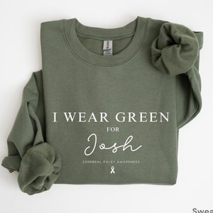 Op de afbeelding: Groen sweatshirt met de tekst "Ik draag groen voor Josh Cerebral Palsy Awareness" en een wit lint.