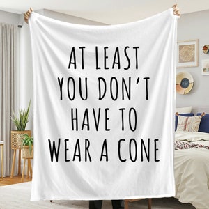 May include: White throw blanket with black text that reads "At least you don't have to wear a cone".