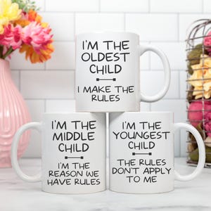 May include: Three white ceramic mugs stacked together, each with a different message in black text. The top mug reads "I'M THE OLDEST CHILD I MAKE THE RULES." The middle mug says "I'M THE MIDDLE CHILD I'M THE REASON WE HAVE RULES." The bottom mug says "I'M THE YOUNGEST CHILD THE RULES DON'T APPLY TO ME."