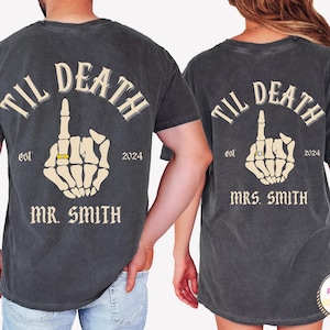 May include: Two charcoal gray t-shirts with the text "TIL DEATH" above a skeleton hand with a ring, the year "2024", and "MR. SMITH" and "MRS. SMITH" below. The shirts have a vintage, distressed look.