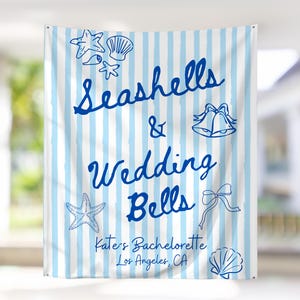 Pode incluir: Uma faixa com listras verticais azuis e brancas. As palavras "Seashells & Wedding Bells" estão escritas em azul. A faixa inclui ilustrações de conchas, estrelas do mar e sinos de casamento. O texto na parte inferior diz "Kate's Bachelorette, Los Angeles, CA."