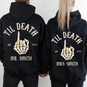 May include: Black hoodies with the text "TIL DEATH" above a skeleton hand giving the middle finger, wearing a ring. The hoodies also read "est 2024" and "MR. SMITH" or "MRS. SMITH".