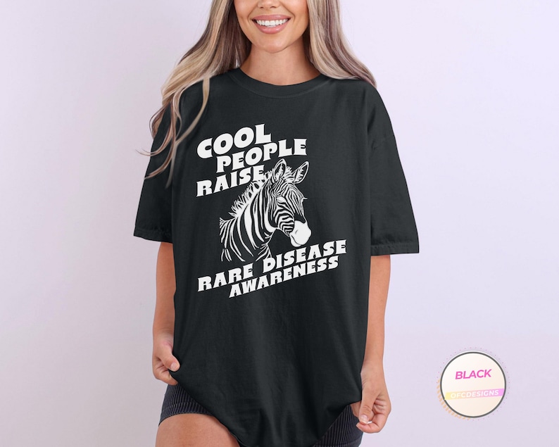 K&ouml;nnte beinhalten: Schwarzes T-Shirt mit wei&szlig;em Text, der "Cool People Raise Rare Disease Awareness" lautet. Neben dem Text ist ein Zebrakopf abgebildet.