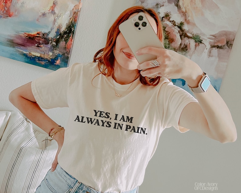 K&ouml;nnte beinhalten: Ein wei&szlig;es T-Shirt mit schwarzem Text, der "YES, I AM ALWAYS IN PAIN." lautet.